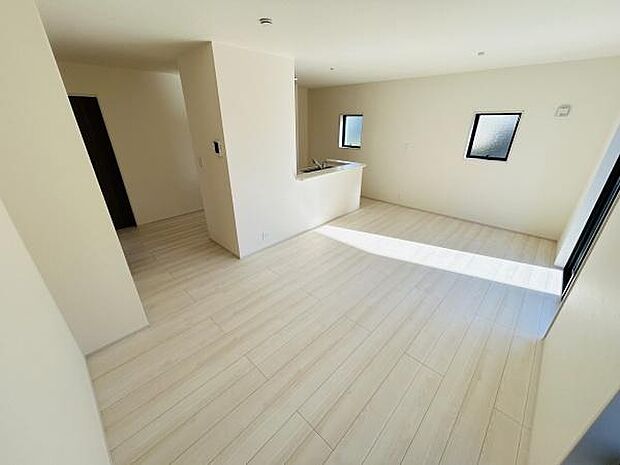 明るい日差しが差し込むリビングです。白を基調とした床と壁が開放感を強調しています。二面採光で室内がより広く感じられます。キッチンとのつながりもスムーズな空間設計です。シンプルなデザインが魅力的です。