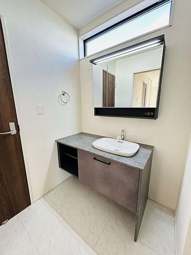 清潔感のある洗面台が設置されています。上部の横長窓から自然光が差し込み明るい空間です。スタイリッシュな鏡とシンプルな洗面ボウルが印象的です。収納スペースも確保されておりすっきりと使えます。