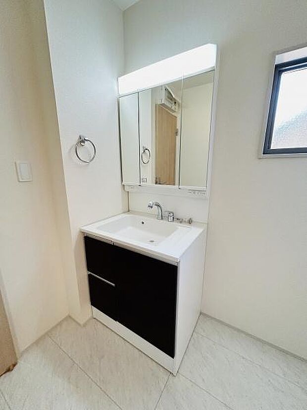 清潔感のあるデザインでシンプルな洗面台が配置されています。ミラーキャビネットが備わっており小物の収納に便利です。壁付けのタオルリングも設置されています。窓から自然光が入る明るい空間です。
