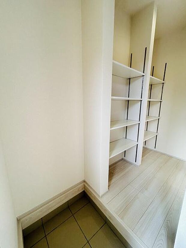 玄関横に設けられた収納棚が広がり使いやすさが感じられる空間です。壁面の明るい色合いが印象的で清潔感があります。床はタイルとフローリングで切り替えられておりメリハリのあるデザインです。