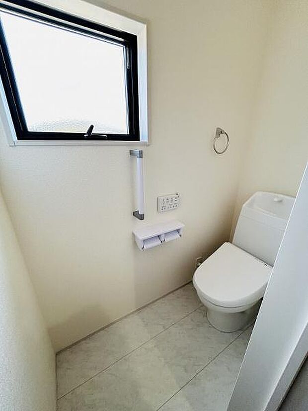 窓が設置されているため換気がしやすいトイレです。シンプルな内装で清潔感があります。手すりとペーパーホルダーリモコン式の設備が備わっています。空間に余裕があり使いやすいレイアウトです。