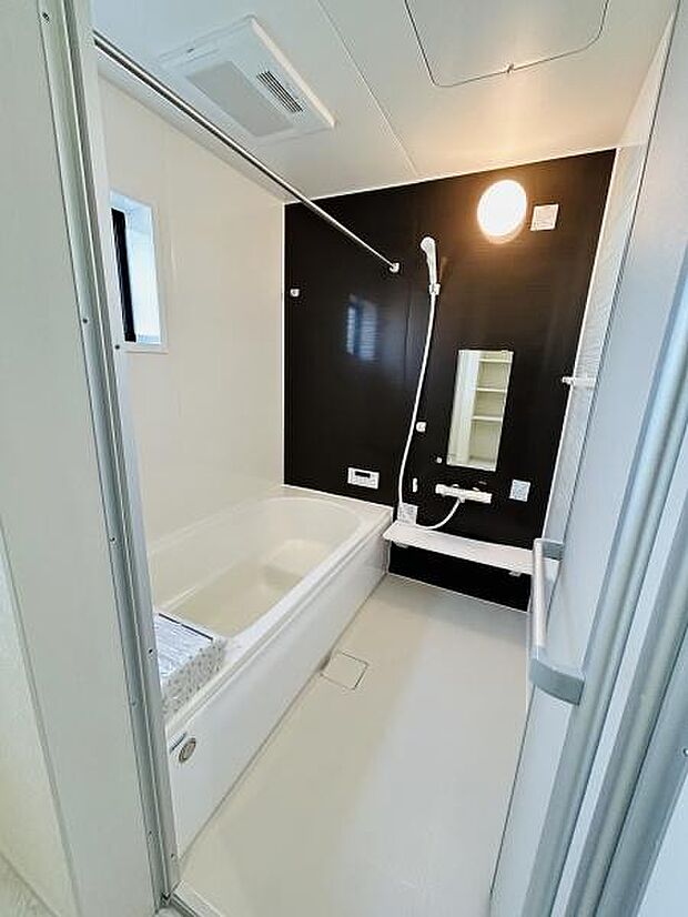 清潔感のある明るい浴室です。浴槽とシャワーが使いやすく配置されています。壁面の配色が空間を引き締めています。換気用の小窓があり湿気対策にも配慮されています。収納棚も設置されていて便利です。