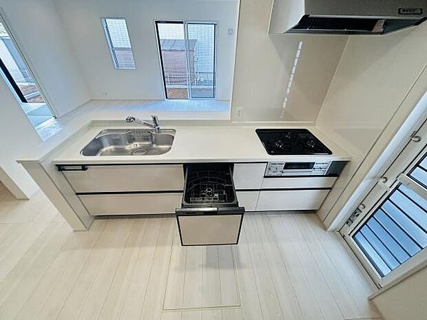 広々としたカウンターとシンクが特徴のキッチンです。3口コンロと食器洗浄機が備わっています。引き出し収納も充実しています。清潔感のあるホワイトカラーが印象的です。窓からの自然光が差し込む明るい空間です。