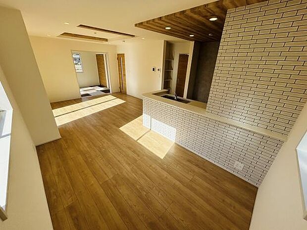 リビングには明るい日差しが差し込み開放的な空間が広がっています。ナチュラルな木目調のフローリングが温かみを演出しています。カウンターキッチンがリビングと自然に調和しています。