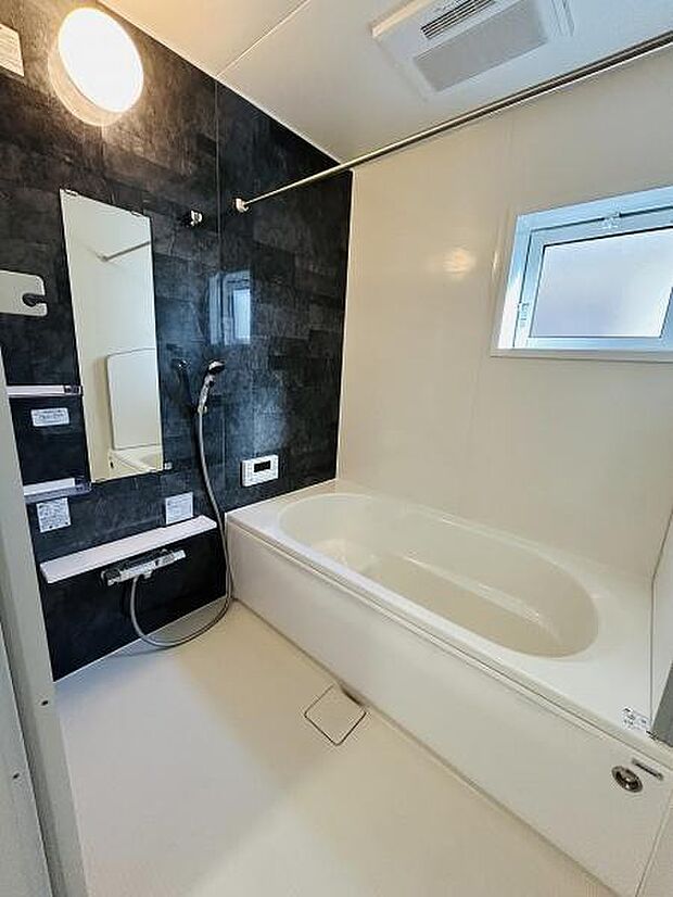 明るい照明が配されたバスルームです。窓があり外からの光や換気が可能です。モノトーンの壁面が引き締まった印象を演出します。広めの浴槽でゆったりとした空間です。シャワーやカウンターも配置されています。