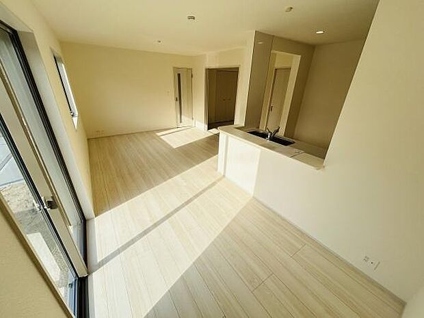 明るい日差しが差し込む開放感のあるリビングです。ナチュラルな床材が空間全体をすっきりと見せてくれます。窓が大きく室内がより広々と感じられます。キッチンとリビングが自然に繋がっている設計です。