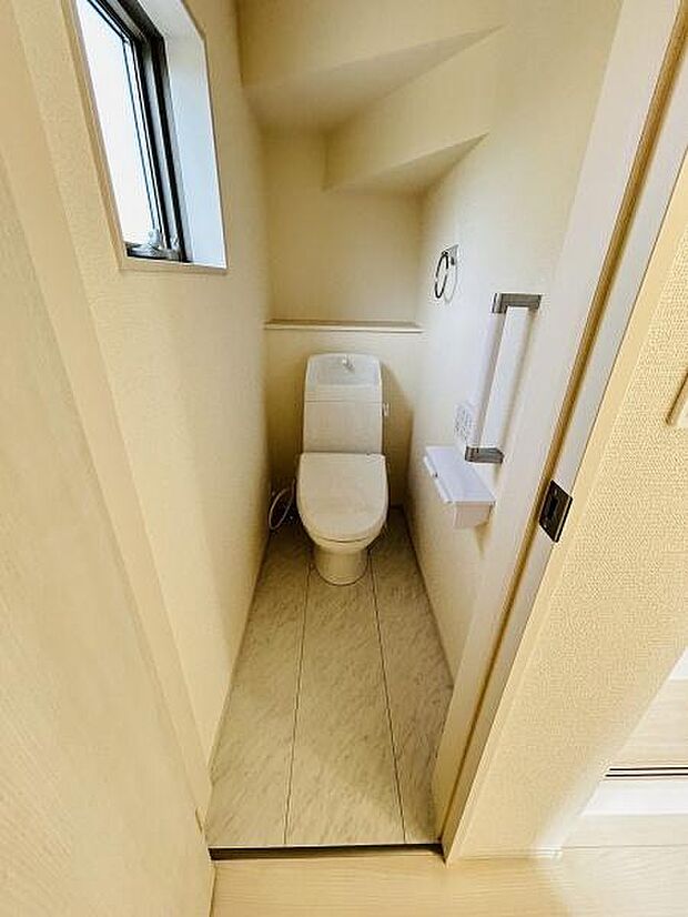 窓から自然光が入る明るいトイレです。手すりが設置されており安心感があります。スペースがすっきりとした印象です。ペーパーホルダーやタオルリングも完備されています。