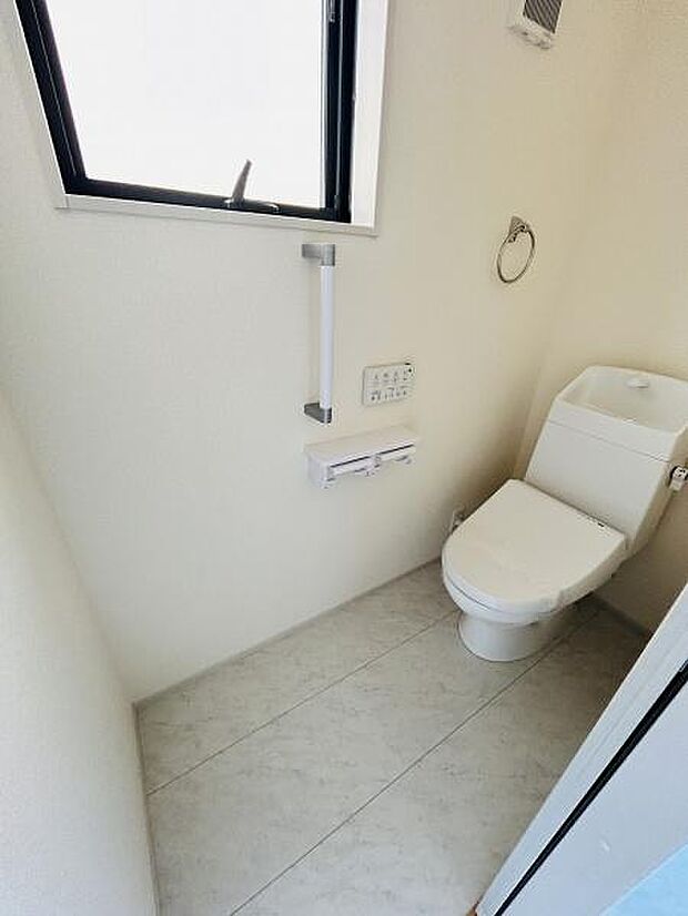 窓があり換気に配慮されたトイレです。手すりが設置されているため安心して利用できます。ペーパーホルダーやリモコンも使いやすい位置に配置されています。清潔感のある空間です。