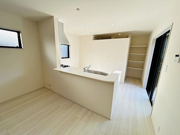 明るいリビング空間が広がっています。白を基調としたインテリアが開放感を演出しています。キッチンとリビングが一体となったレイアウトが印象的です。収納棚も備わっており室内がすっきりと保てます。