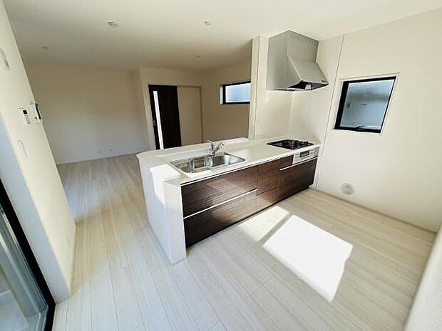 シンプルで洗練されたデザインのキッチンです。対面型で空間にゆとりがあります。明るい色合いの床が全体をすっきりと見せます。窓から自然光が差し込むため室内も明るい印象です。収納スペースも備わっています。