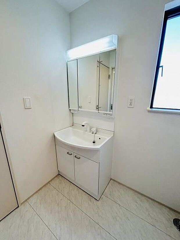 シンプルで使いやすい洗面台が設置されています。明るい照明付きのミラーが特徴です。清潔感のある内装が空間を広く見せています。収納スペースがあり整理整頓に便利です。窓があり換気もしやすい設計です。