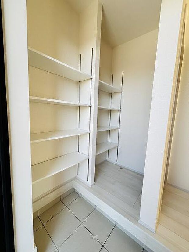 棚が複数設置されており小物や日用品などを整理しやすい収納空間です。奥行きがありさまざまなアイテムに対応可能です。明るい色合いで清潔感があります。床の段差がアクセントとなり使い勝手に配慮されています。