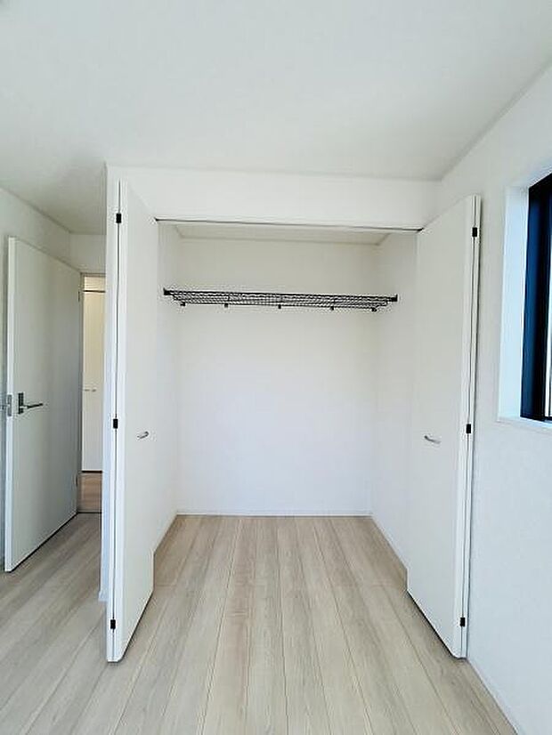 シンプルなデザインの収納スペースです。奥行きのあるクローゼットで使い勝手が良いです。棚やハンガーパイプが設置されており収納力を感じられます。明るい色味の床で室内が開放的に見えます。