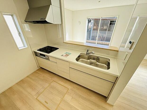 窓から光が差し込む明るいキッチンです。カウンター付きで開放感があります。設備がすっきりまとまっており使いやすい設計です。収納スペースも充実しています。清潔感のあるデザインです。