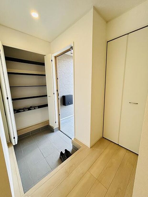 玄関は明るい照明が印象的です。広々としたシューズラックがあり整理整頓がしやすそうです。クローゼットも設けられており収納スペースが豊富です。床の配色が落ち着いた雰囲気を演出しています。