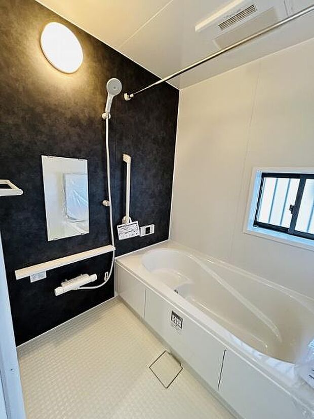 シンプルで清潔感のあるバスルームです。モノトーンの配色が空間を引き締めています。使い勝手の良い手すりや浴槽が設置されています。室内に窓があり自然光を取り入れられます。浴室乾燥機もついています。