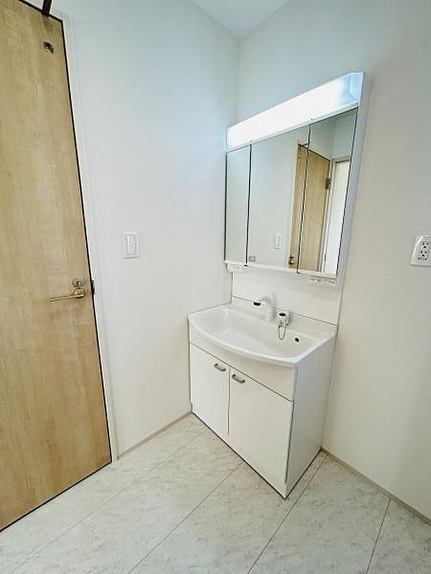 清潔感のある洗面台ですっきりとした空間です。ミラーキャビネットが収納力を高めています。明るい照明付きで使い勝手の良い洗面所です。床は汚れが目立ちにくいデザインとなっています。