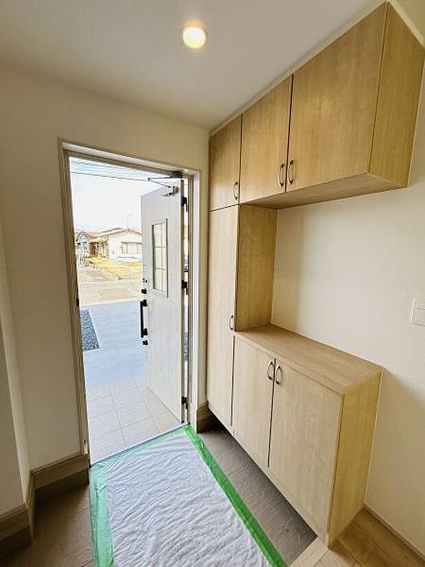 明るい玄関スペースで収納棚も備わっています。ナチュラルカラーの木目調が印象的です。シンプルな空間で室内全体がすっきりとした印象になります。玄関ドアからの光の入り方もポイントです。