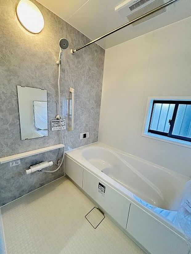 明るい照明と大きな窓で開放感のある空間です。浴槽はゆったりとしたサイズでグレーの壁面が落ち着いた雰囲気を演出します。清潔感のある内装でお手入れも簡単です。シャワーや鏡も使いやすい配置になっています。