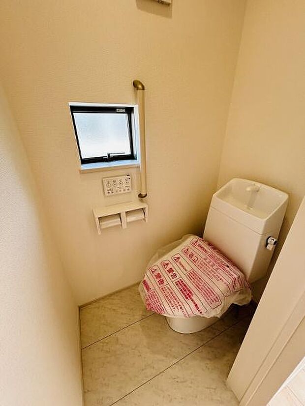 コンパクトな空間に設置されたトイレです。窓があり換気や採光が確保されています。手すりが備え付けられており使いやすさに配慮されています。ペーパーホルダーも2連タイプで便利です。