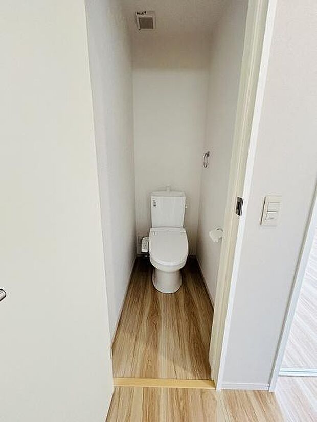 木目調の床が明るい印象を与えるトイレです。室内は清潔感がありシンプルなデザインとなっています。スペースがしっかり確保されており使いやすさにも配慮されています。