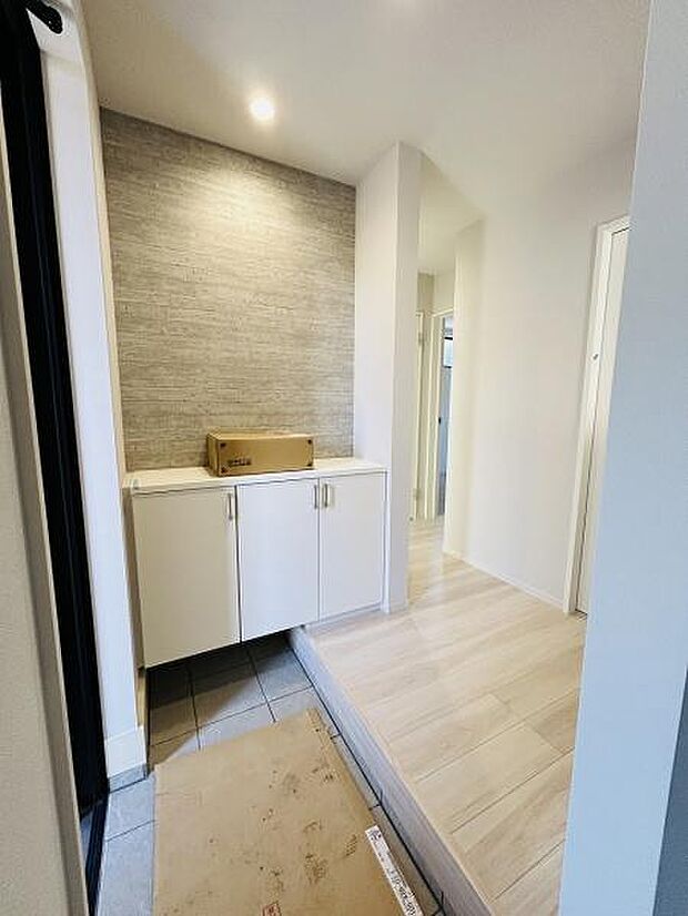 玄関部分は明るくすっきりとした空間です。収納スペースが備わっており整理整頓がしやすい仕様です。石目調のアクセント壁がポイントとなっています。フローリングとタイルの切り替えが印象的です。