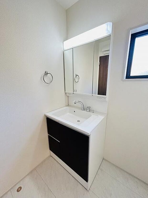 シンプルなデザインの洗面台が設置されています。大きな鏡は空間を広く見せ毎日の使用に便利です。収納スペースも備わっているため日用品の整理がしやすいです。窓があることで洗面所に明るさが確保されています。