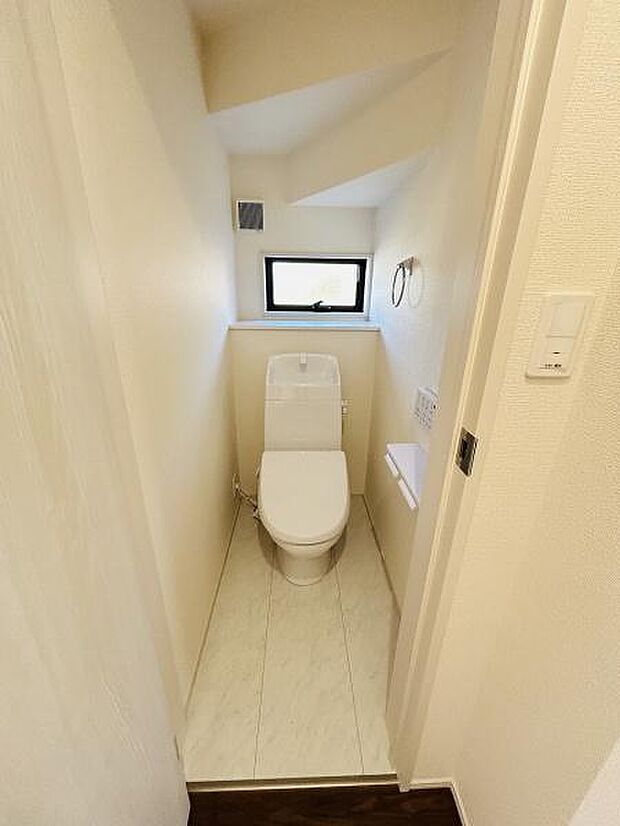 コンパクトな空間ながら窓があり換気しやすいトイレです。シンプルな内装で落ち着いた雰囲気です。壁側にはペーパーホルダーやタオルリングが設置されています。トイレ本体も清潔感があります。