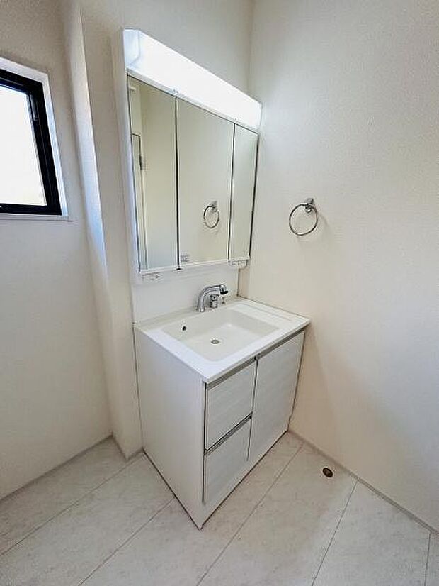 シンプルで清潔感のある洗面台が配置されています。大きな三面鏡が付属しており身だしなみの確認に便利です。収納スペースも豊富にあり小物の整理がしやすい仕様です。