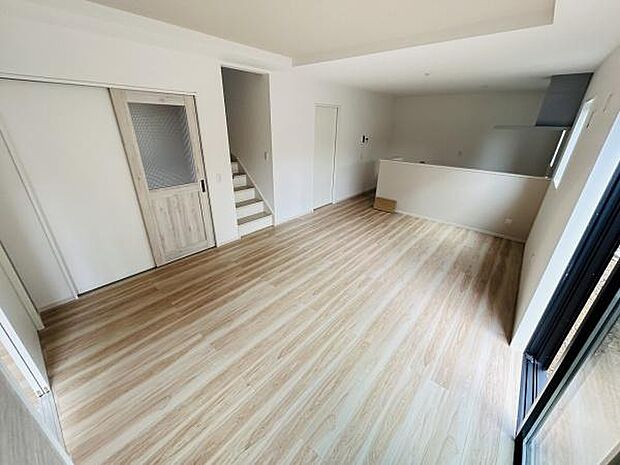 リビングは明るく開放感がありナチュラルなフローリングが特徴です。窓が大きく採光性も良好です。室内はシンプルな設計で家具の配置がしやすい空間です。隣接する階段や出入口もすっきりとしたデザインです。