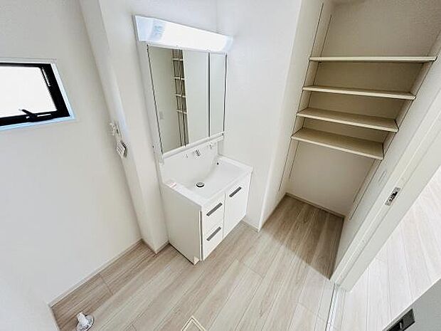 洗面台がすっきりとした印象で明るい室内に溶け込んでいます。隣には収納棚があり日用品の整理に役立ちます。床は落ち着いた色合いでお手入れもしやすそうです。窓があるため換気に配慮されています。