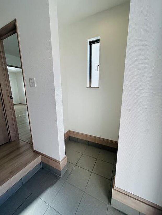 玄関にスリット窓があり光がしっかりと差し込みます。清潔感のあるタイル床が特徴です。シンプルな空間がすっきりとした印象を与えます。木目の建具との調和が穏やかです。