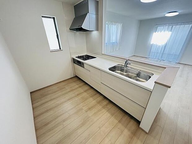 明るい色合いの床材とシンプルなデザインのキッチンが特徴です。窓があり換気もしやすい造りです。IHコンロと広めのシンクが備わっています。リビングとのつながりが感じられる間取りです。