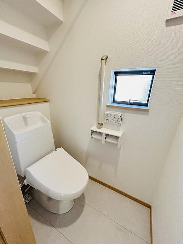 手すり付きで安心感のあるトイレです。小窓が設けられており換気や明るさも確保できます。空間を有効活用したレイアウトになっています。収納棚もあり整理整頓しやすい設計です。内装がシンプルで清潔感があります。