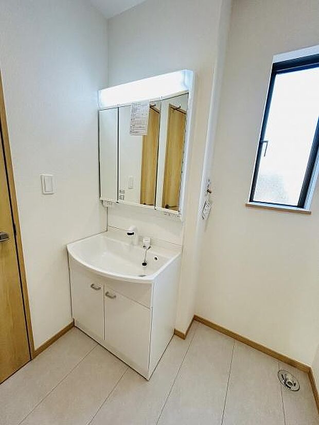 清潔感のある洗面台が設置されています。収納が備わっているため洗面用品の整理に役立ちます。大きな鏡で身支度もスムーズに行えます。明るい照明が手元をしっかり照らします。窓があるので換気もしやすいです。