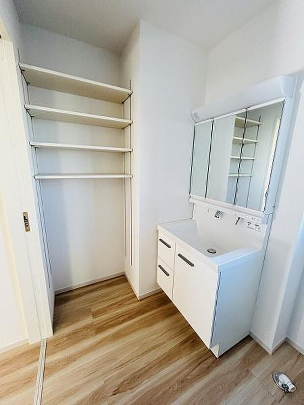 ホワイトを基調とした明るい空間が印象的です。扉付き収納と洗面台がコンパクトにまとまっています。床材の木目調デザインがすっきりとした雰囲気を演出しています。可動棚付きで収納力も確保されています。