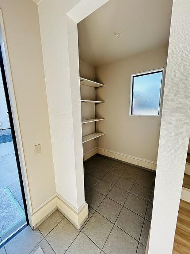 窓があり明るい雰囲気の収納スペースです。棚板が複数設置されていて整理しやすい仕様です。タイル床でお手入れも簡単です。アーチ状の開口部がアクセントになっています。玄関付近に位置しており便利です。