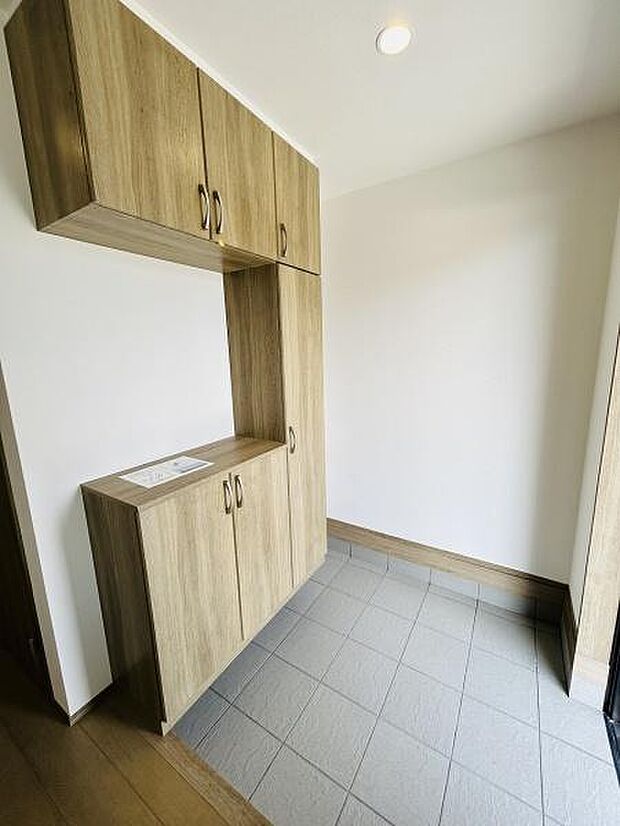 玄関には収納が充実しており使いやすいデザインです。木目調のキャビネットが空間に落ち着いた印象を与えています。広めのタイルスペースでお手入れも簡単です。明るい室内で清潔感があります。
