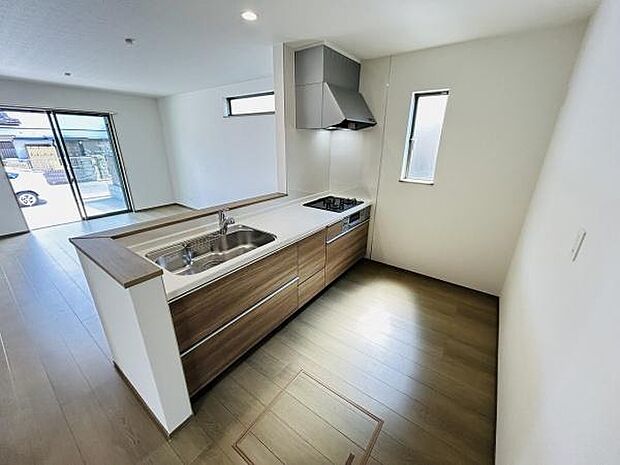 木目調のデザインが際立つシステムキッチンです。カウンターとシンクが一体型で作業動線もスムーズです。窓からの採光により日中は明るい空間が広がります。リビングとの一体感が感じられるレイアウトです。