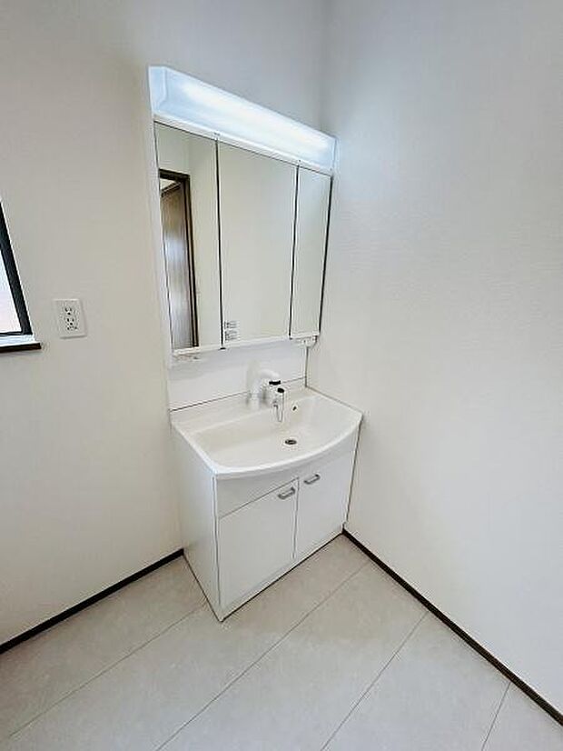 洗面台はシンプルなデザインで周囲と調和しています。三面鏡仕様で使い勝手が良い印象です。収納スペースもしっかりと確保されています。洗面所は明るい雰囲気となっています。清潔感のある空間が広がっています。