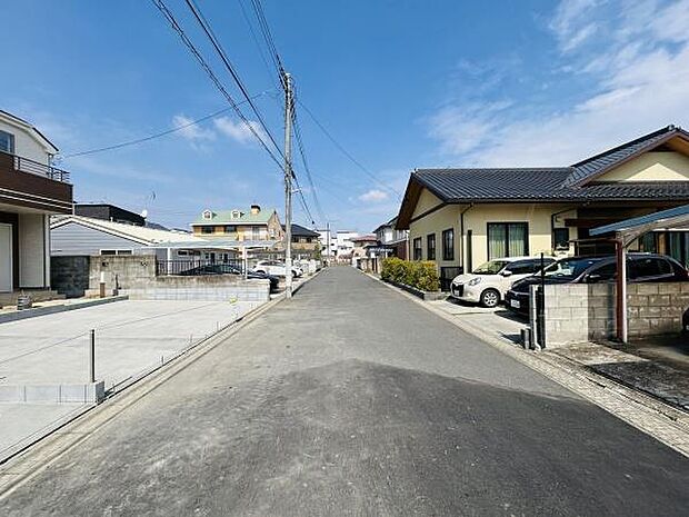 前面道路が広がり車の出入りがしやすい環境です。周辺に住宅が並び整然とした街並みが特徴です。現地の様子が一目でわかる写真で安心感があります。青空が広がり明るい印象の現地写真です。