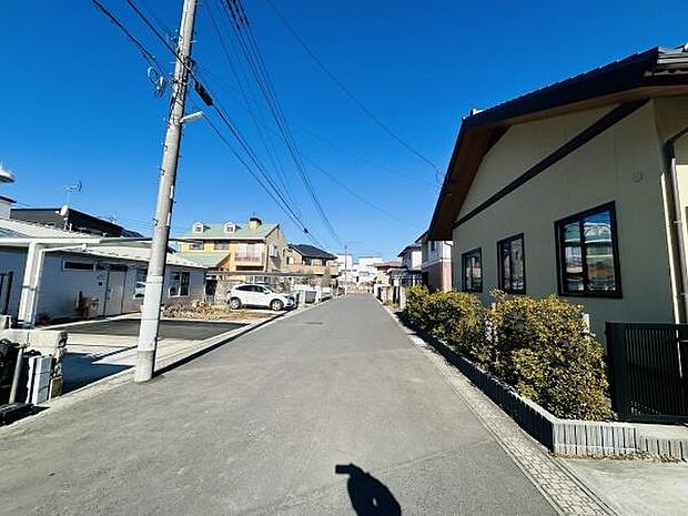 前面道路は広々としており車の通行もスムーズに感じられます。周辺は住宅が立ち並び街並みに統一感があります。日当たりの良さも印象的で開放的な雰囲気です。電柱や配線も整然と配置されています。
