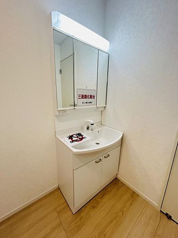 三面鏡が備え付けられており収納スペースが充実しています。洗面台はシンプルなデザインでお手入れもしやすい仕様です。床は明るい木目調で全体的に清潔感のある空間となっています。