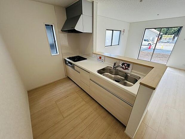 キッチンは明るい木目調の床と調和し清潔感があります。シンクと調理スペースがゆったりしており動線もスムーズです。小窓が配置されているため自然光が差し込みます。リビングへの見通しも良好です。