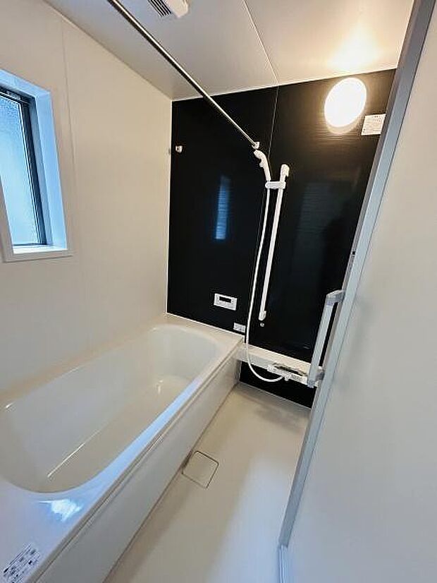 シンプルなデザインで清潔感のあるバスルームです。壁面のカラーアクセントが落ち着きある空間を演出します。使いやすい手すりと広めの浴槽が特徴的です。浴室に窓があり換気や採光にも配慮されています。