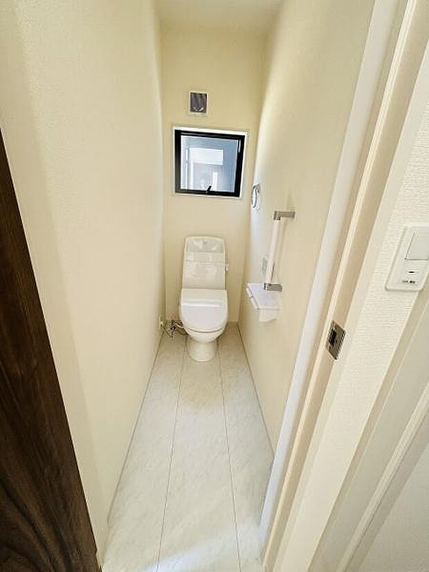 シンプルなデザインのトイレ空間です。窓付きで換気がしやすい設計となっています。ペーパーホルダーやタオルリングなどの設備も備え付けられています。清潔感のあるフローリングが魅力です。