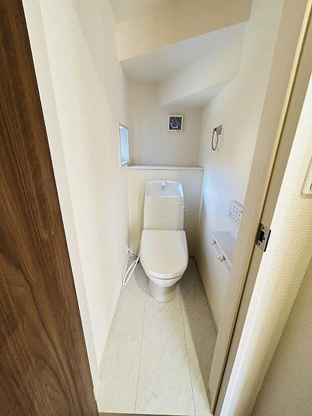 清潔感のある内装でコンパクトにまとまったトイレです。壁面には小窓があり圧迫感を軽減しています。収納や設備もシンプルに配置され日々のお手入れも容易です。