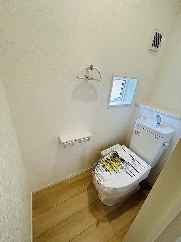 シンプルで清潔感のあるトイレ空間です。小窓から自然光が入り明るい印象です。ペーパーホルダーやタオル掛けも設置されています。コンパクトながらも使い勝手が良さそうです。