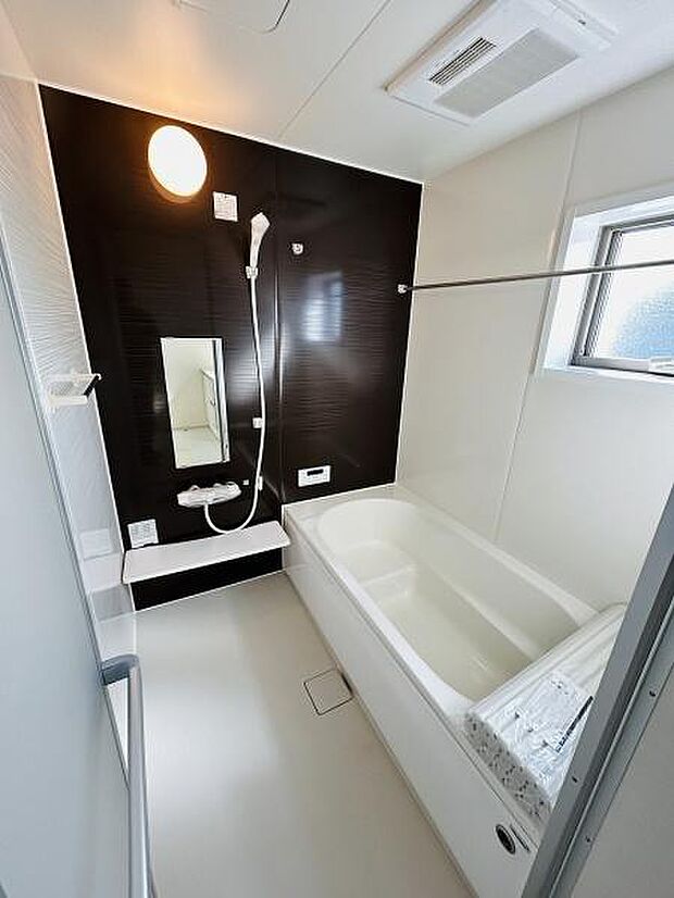 シンプルで使いやすいデザインのバスルームです。窓があり換気しやすく明るい空間が広がっています。浴槽やシャワー周りも清潔感があります。壁面はアクセントカラーで落ち着きのある印象です。