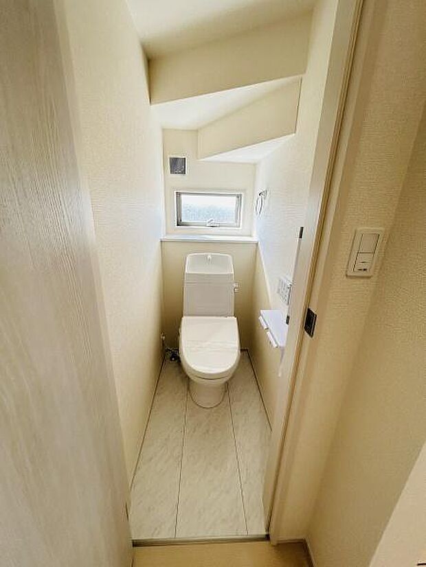 窓付きのトイレは明るさを感じられる空間です。シンプルながら清潔感を重視したデザインです。壁のクロスと床の明るい色合いが印象的です。換気にも配慮されたレイアウトです。